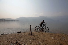 Un bambino nepalese appartenente all'etnia Chhetri ed alla casta Vaisya pedala con la sua bicicletta nelle acque del lago di Phewa Tal, Pokhara, Nepal 2018