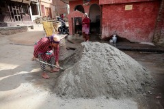 Una donna manovale Newari affonda la pala nel cemento che porterà a piedi per quattro piani nell'edificio in ricostruzione dove lavora, con l'ausilio della grande cesta ("Doko") che isserà sulla schiena, villaggio di Kirtipur, Nepal 2018.