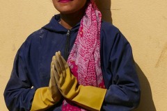 Una giovane donna di etnia Sherpa mi saluta congiungendo le mani nel tradizionale saluto "Namasté" (mi inchino alla Divinità che risiede in te), in un momento di pausa durante il duro lavoro come manovale: per non rovinarsi le dita utilizza i guanti ed un lungo foulard le copre i capelli, ma la sua eleganza innata resta intatta. Villaggio di Bungamati, Nepal 2018.