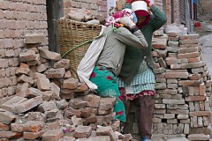 Il momento in cui queste donne Newari issano sulla schiena il "Doko" (la grande cesta piena di mattoni), sistemando sulla fronte la lunga fascia che equilibra il peso poco prima di portarli sulle scale dell'edificio in ristrutturazione, villaggio di Kirtipur, Nepal 2018.