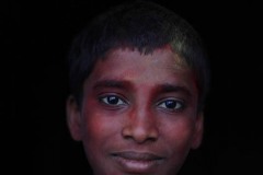 Ritratto di Chadrabhushan, un ragazzo Hindu di 16 anni che è giunto con la sua famiglia sino al villaggio di Saundatti dal lontano villaggio di Kuchipudi in cui vive. Anche lui porta i "segni" della partecipazione al Renuka Yallamma Jatra, i festeggiamenti in onore della Dea Yallamma (dea della fertilità, conosciuta anche come Jagadamba, la Madre dell'Universo): sui capelli, sul viso e sui vestiti si è depositata la polvere gialla e rossa della curcuma e del kum kum. Regione del Karnataka, India 2015.