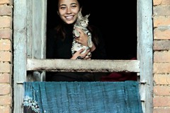 Dalla sua casa una giovane nepalese (appartenente all'etnia Gurung) si affaccia alla finestra con il suo gattino, villaggio di Gorkha, Nepal 2018.