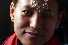 Una giovane devota nepalese di etnia Gurung, appena uscita dal Tempio di Bhimsen, nella piazza principale della città di Pokhara: al termine della Puja (l'atto di adorazione nei confronti di una particolare forma della Divinità che può esprimersi in un'offerta, detta "Upachara", un culto, una cerimonia e un rito. Tradizionalmente essa si esegue al cospetto di una "Murti", ovvero una rappresentazione fisica del Dio che si intende adorare. La celebrazione della puja, in genere, è accompagnata dal canto di mantra o di inni sacri e spesso prevede il lavacro e l'unzione dell'idolo, oltre alle offerte di doni destinati alla Divinità che, nel caso di alimenti verranno poi consumati dall'offerente, in quanto dopo il rituale essi divengono "Prasada", cioè cibo benedetto e purificato), ha posto sulla fronte i chicchi di riso offerti al Dio mescolati con la pasta di sandalo, quale segno di buon auspicio dato che, ora, quei chicchi sono stati consacrati dalla benevolenza della Divinità. Nepal 2018.