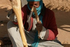 Uomo Haoussa modella un bastone di legno utilizzando uno strumento simile ad uno scalpello, Villaggiio di Dabaga, Niger 2020