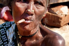 Una anziana donna Kodavas fuma foglie di tabacco arrotolate mentre riposa accanto alla sua capanna nel villaggio di Kakkabe: gli orecchini posti su entrambe le narici costituiscono una caratteristica peculiare delle donne di questa etnia. Regione del Karnataka, India 2015.
