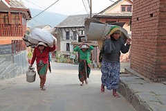 Lungo la strada principale di Bandipur, l'incantevole città Newari nepalese, dove si susseguono tradizionali case a schiera, le donne Newari trasportano incredibili pesi sulla schiena senza grandi sforzi apparenti, Nepal 2018