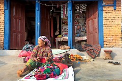 Una bottega artigiana dove una donna nepalese di ertnia Newari crea, utilizzando una vecchia macchina da cucire a manovella, delle borsette in tessuto. Mentre la suocera è all'interno del negozio che mi osserva. Bandipur, Nepal 2018