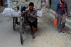 In un vicolo nella città vecchia di Kathmandu uno Sherpa trascina a piedi faticosamente sul suo ciclo risciò un carico pesantissimo con sacchi che contengono merce da consegnare ai vicini negozi del quartiere Thamel, Nepal 2018