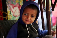 Un bambino nepalese appartenente alla casta dei "sudra" (servi o artigiani) con un pacchetto di biscotti che stringe nella mano fa merenda seduto sul sedile sgangherato del risciò che il padre, di nome Bir Bahadur e di etnia Tamang, affitta dal proprietario del mezzo pagandolo 50 rupie al giorno (circa 5 euro) e guadagnando, girando come un pazzo per le strade caotiche e super inquinate di Kathmandu, circa 500 rupie; ora il risciò è fermo, senza clienti ed il bimbo, di nome Rajiv (che significa fiore di loto blu, un fiore legato alla purezza del corpo e dell'anima) può restare seduto tranquillamente, dintorni di Durbar Square, Kathmandu, Nepal 2018