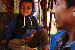 Un piccolo bambino nepalese appartenente alla casta dei "Sudra" (servi o artigiani) con un pacchetto di biscotti che stringe nella mano fa merenda seduto sul sedile sgangherato del risciò che il padre, di nome Bir Bahadur e di etnia Tamang, affitta dal proprietario del mezzo pagandolo 50 rupie al giorno (circa 5 euro) e guadagnando, girando come un pazzo per le strade caotiche e super inquinate di Kathmandu, circa 500 rupie; ora il risciò è fermo, senza clienti ed il bimbo, di nome Rajiv (che significa fiore di loto blu, un fiore legato alla purezza del corpo e dell'anima) può restare seduto tranquillamente sorridendo al padre, dintorni di Durbar Square, Kathmandu, Nepal 2018.