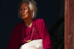 Una anziana donna Tamang è seduta sull'uscio della sua abitazione ed osserva il movimento delle persone in strada: presenta una perforazione della narice con l'inserimento di un orecchino (applicato in giovane età) e la perforazione del setto nasale con inserimento di un altro orecchino (a simboleggiare l'appartenenza al proprio sposo), villaggio di Nagarkot, Nepal 2018.