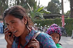 Una donna di etnia Thakali parla al cellulare trasportando il suo bambino sulla schiena (che mi osserba curioso) mentre è in attesa di imbarcarsi su una Doonga (barca a remi), lungo lago di Phewa Tal, Pokhara, Nepal 2018