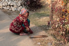 Una anziana donna Tharu pulisce il giardino antistante la sua capanna con una piccola scopa da lei stessa realizzata legando delle fibre vegetali di una pianta della vicina foresta, villaggio di Harnari, Chitwan National Park, Nepal 2018.