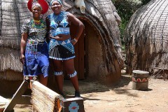 Due giovani donne Zulu si abbracciano nel cortile antistante alle loro capanne, Villaggio Lesedi, Sud africa