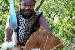 Guerriero Zulu con il tipico copricapo a fascia ("Umqhele") ricavato dalla pelle dell'Impala e realizzato con un tubo di pelliccia imbottito con sterco di vacca o fibre vegetali, indossa inoltre le piume di struzzo ("Upaphe") e stringe tra le sue mani la corta lancia con la punta larga come una sciabola ("Assegai") ed il grande scudo rivestito di pelle di vacca ("Isihlangu"), il torace è parzialmente coperto da una casacca di pelle di leopardo, Villaggio Shakaland, Sud Africa 2012