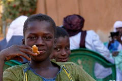 Sguardo compiaciuto, durante la Festa di fidanzamento ad un gruppo di bambini bisognosi viene offerto del pane da parte della famiglia Tuareg che celebra la promessa sposa, mentre gli invitati chiaccherano serenamente, Niamey, Niger 2020