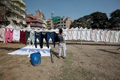 Cheetrapati, un quartiere di Kathmandu dove si concentrano le lavanderie a cielo aperto: uomini e donne, dopo aver lavato a mano i diversi capi di abbigliamento, li stendono sull'erba o su lunghi fili appositamente fissati a pali di legno per farli asciugare. Kathmandu, Nepal 2018