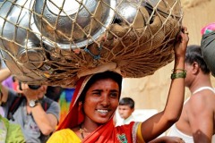 Una donna Hindu ha appena acquistato queste suppellettili in alluminio nell'affollato mercato di Saundatti e le trasporta tranquillamente sul capo con nonchalance lungo le strade affollate di pellegrini: Dintorni del villaggio di Saundatti, Re3gione del Karnataka, India 2015.