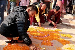 Sul piazzale antistante al Guru Lhakhang Monastery di Bodhnath, un monaco, coadiuvato da alcuni fedeli, crea disegni floreali sulla pavimentazione prima dell'avvio della Cerimonia Chakra Darma, Nepal 2018