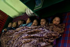Dopo pranzo i bambini vengono messi a dormire su un materassino e coperti con un telo comune: non tutti però chiudono subito gli occhi per riposare, c'è chi si guarda in giro, chi osserva il soffitto, chi si concentra per trovare il modo di prendere sonno, Shree Bal Bikosh Basic School di Cheetrapati nella capitale Kathmandu, Nepal 2018