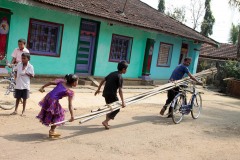 Nel villaggio rurale di Belur due bambini aiutano il papà nel trasporto di alcune lunghe canne di bambù: le autovetture o i trattori ancora non esistono in questa realtà e ci si muove a piedi o in bicicletta. Regione del Karnataka, India 2015.