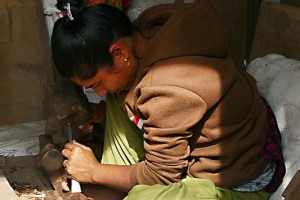 Una giovane donna Newari intaglia il legno con martello e scalpello nella sua piccola bottega lungo la strada principale del villaggio di Khokanà, Nepal 2018.