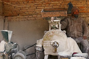 Un piccolo laboratorio dove di macina il granturco trasformandolo in farina (un mulino in miniatura): l'uomo Newari seduto attende clienti per rimettere in moto i macchinari. Villaggio di Bungamati, Nepal 2018.