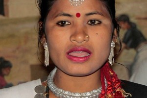 Primo piano di una ballerina Tharu che canta: i monili che indossa con eleganza e la piuma di pavone tra i capelli rappresentano i segni distintivi della tradizione e della cultura di questo Popolo dalle antichissime origini. Villaggio di Sauraha, Chitwan National Park, Nepal 2018.