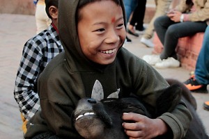 Un bambino di strada dal volto raggiante di gioia accarezza un vitellino nella centralissima Durbar Square di Kathmandu, Nepal 2018