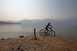 Un bambino nepalese appartenente all'etnia Chhetri ed alla casta Vaisya pedala con la sua bicicletta nelle acque del lago di Phewa Tal, Pokhara, Nepal 2018