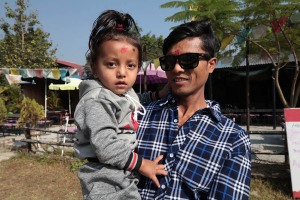 Ritratto di una bambina in braccio al suo papà: lei mi guarda curiosa ed interrogativa. Appartiene, insieme al padre, all'etnia Thakali ed il suo nome è Mahadevi (letteralmente la "grande Dea", lungo lago di Phewa Tal, Okhara, Nepal 2018.