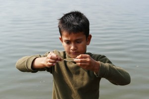 Un bambino di etnia Newari pesca i pesciolini del lago con le mani: qui sta osservando il suo "trofeo" molto compiaciuto e concentrato (la sua è una storia non proprio allegra, perde entrambi i genitori ed ora abita con il fratello più grande che lavora e lo mantiene agli studi), lago di Phewa Tal, Pokhara, Nepal 2018.