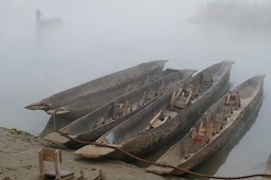 Nella fitta nebbia dell'alba una barca condotta da un esperto uomo Tharu si allontana con il suo carico di turisti lungo le acque brumose del fiume Rapti, Chitwan National Park, Nepal 2018.