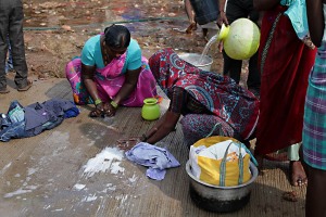 Alcune donne Hindu lavano i propri indumenti strofinandoli con il sapone su una grande stuoia in corda intrecciata da loro stessa creata: non avendo acqua corrente utilizzano bacinelle ed anfore per risciacquarli, accampamento nei dintorni del villaggio di Saundatti, Regione del Karnataka, India 2015.