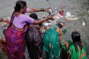 Nella piscina naturale alimentata dal Saundatti Lake, una mamma Hindu bagna con la piccola anfora in metallo le due figlie per eseguire il rito di purificazione attraverso il bagno sacro. L'acqua, la terra ed il fuoco sono i tre elementi naturali sui quali si basa la loro vita quotidiana ed il loro credo religioso. In occasione della Festa dedicata alla Dea Yallamma (Renuka Yallamma Jatra) costituiscono le tre tappe fondamentali per giungere alla purificazione del corpo e dell'anima. Dintorni del villaggio di Saundatti, Regione del Karnataka, India 2015.