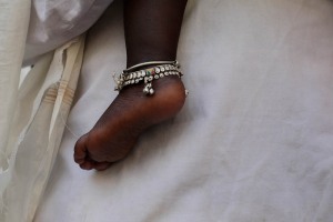 Primo piano del piedino di una bimba, mentre è in braccio alla sua mamma durante la processioine in onore della Dea Yallamma: spiccano le due cavigliere in argento che adornano la caviglia. Dintorni del Temnpio dedicato alla Dea Yallamma, villaggio di Saundatti, Regione del Karnataka, India 2015.