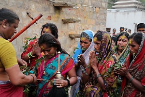 Un eunuco (o transgender, ovvero transessuale o castrato, definito dagli Hindu "hijra", cioè impotente) sta distribuendo dei ramoscelli di Neem, pianta considerata sacra, alle fedeli in fila vicino all'ingresso del Tempio dedicato alla Dea Yallamma. In passato gli eunuchi erano considerati stimati sacerdoti della Dea Yallamma (Dea della fertilità) e venerati come figure sacre. L'identità dell'eunuco risale al IV secolo d.C. (è compresa nel testo del Kamasutra) e si incarna nel sacerdote devoto alla Dea Kali che, a sua volta, si identifica con la Dea Yallamma. Il rito di iniziazione, che consiste nella castrazione senza anestesia, viene effettuato in totale segreto. La colonizzazione britannica è all'origine dell'emarginazione di una delle più grandi ed antiche comunità transgender del mondo: nel 1897 venne emanata una legge che dichiarava illegali le pratiche omosessuali. Da allora, con alterne vicende, gli Hijra (che attualmente si aggirano attorno ai tre milioni di individui in India), sono segregati nelle baraccopoli dei centri urbani più importanti (come Chennai, Bombay o Nuova Delhi) e si guadagnano da vivere cantando e ballando alle cerimonie private (matrimoni ed altre ricorrenze o festività), assicurando con la loro presenza la migliore benedizione per un futuro prospero alla famiglia che li ha invitati. La maggior parte di loro, però, è costretta a mendicare od a prostituirsi con effetti devastanti per l'alto tasso di contrazione dell'Hiv. Villaggio di Saundatti, Regione del Karnataka, India 2015.