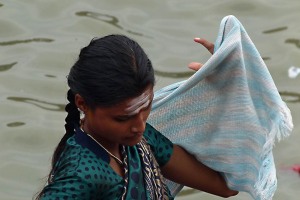 Una giovane donna Hindu si sta asciugando dopo il bagno rituale di purificazione: sulla sua fronte è evidente il "Tilaka" tipico dei seguaci di Shiva che prende il nome di "Tripundra". Consiste in tre strisce orizzontali di pasta di "vibhuti" (cenere consacrata) di colore bianco crema tra le quali, al centro, viene posto un piccolo cerchio rosso di pasta di sandalo e di kum kum (una polvere rossa a base di curcuma e calce spenta. Piscina alimentata dal Saundatti Lake, villaggio di Saundatti, Regione del Karnataka, India 2015.
