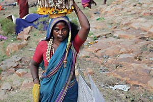 Una sciamana Hindu porta sul capo la statua riproducente l'immagine della Dea Yallamma realizzata in argilla ricoperta da una lastra di argento. Il suo nome è Jyotsna ed è considerata l'incarnazione terrena della Dea Yallamma (e da quest'ultima investita di poteri speciali e facoltà guaritrici superiori). La sua forza discende direttamente dalla grande Madre dell'Universo (che si identifica con la Dea Yallamma e che viene denominata anche con il termine Jagadamba), la Divinità che la possiede durante la trance e attraverso la quale opera nei confronti dei devoti. Nel rituale della guarigione, ad esempio, la sciamana "succhia" letteralmente dal corpo del posseduto il male, sputandolo poi fuori. Questi oracoli (tali possono essere considerati gli sciamani) usano il proprio corpo come simbolo del sacro e veicolo di forze suscitate da un'esperienza visionaria prima ancora che mistica. Posseggono la forza primordiale di ogni essere umano al di là del bene e del male così come socialmente codificati, qualcosa che attrae e respinge, affascina ed ammutolisce. Dintorni del Tempio dedicato alla Dea Yallamma, villaggio di Saundatti, regione del Karnataka, India 2015.