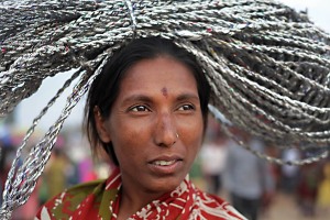 Primo piano di una donna Hindu che vende, tra la folla che si accalca nel mercato di Saundatti, un fascio di corde da lei stessa realizzata: il suo nome è Chameli. La sua non è una vita semplice e serena: è una Dalit o Paria (in sanscrito significa oppressa), cioè una "intoccabile". Chi non appartiene, come lei, alle quattro caste riconosciute, va evitato, emarginato, non può essere mai toccato perchè considerato impuro. Secondo la leggenda Hindu, se qualche antenato era stato un peccatore (la cui anima si reincarna con la finalità di purificarsi nelle generazioni successive) tutti i discendenti appartenevano ai fuori casta e dovevano accettare il loro destino di subordinazione. Soprattutto nelle zone rurali dell'India, in cui il peso delle tradizioni risulta più radicato e le angherie delle caste alte più diffuse, i Dalit vivono esistenze da cittadini inferiori, ai quali viene negato l'accesso ai pozzi, la proprietà terriera, l'interazione con gli appartenenti alle caste elevate, l'istruzione ed il ricorso alla sanità. Nel caso di mancato rispetto di questi obblighi da parte dei Paria, la pena crudele ed immediata da parte del popolo è il linciaggio. Ma l'espressione serena e fiera, dignitosa e quasi austera di Chameli sembrano farle dimenticare, almeno per un attimo, il suo passato, il suo presente ed il suo futuro. Regione del Karnataka, India 2015.