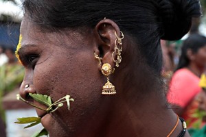Primo piano di Godavari, un eunuco o transgender (denominato anche"Hijra" dagli Hindu che significa impotente): sul naso e sulle orecchie indossa un numero incredibile di orecchini d'oro, mentre tra le labbra stringe un ramoscello di una pianta considerata sacra che prende il nome di Neem (come segno di penitenza e devozione nei confronti della Dea Yallamma). In passato gli Hijras erano considerati quasi delle semidivinità e svolgevano il ruolo di stimati sacerdoti della Dea Yallamma (Dea della fertilità). Oggi transgender ed eunuchi sopravvivono cantando e ballando ai matrimoni o ad altre cerimonie assicurando con la loro presenza benedizioni e un futuro prospero per la famiglia che li ha ospitati. Ma un numero sempre maggiore è costretta a chiedere l'elemosina o, ancor peggio, a prostituirsi. Dintorni del villaggio di Saundatti, regione del Karnataka, India 2015.