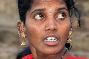 Ritratto di una giovane donna Hindu di nome Harinakshi: tra le sopracciglia indossa il "Bindi" (tradizionalmente consiste in un punto rosso che in sanscrito significa goccia, particella, punto, considerato il terzo occhio; in questo caso, però, è un gioiello utilizzato come decorazione per la fronte). Inoltre indossa anche gli orecchini d'oro "Jhumka", gli ornamenti che, secondo la tradizione, servono ad impedire che gli spiriti maligni, in grado di entrare nel corpo attraverso una delle sue aperture e prenderne il controllo, passino attraverso l'orecchio (considerato la parte nobile del corpo, segno di sviluppo spirituale). Gli Jhumka hanno una particolare forma: riproducono una piccola campana. Sono piuttosto pesanti e quindi vengono sostenuti da una piccola catena (chiamata "Sahaara") fissata nella parte posteriore dell'orecchio o sui capelli. La medicina dell'agopuntura attribuisce agli orecchini un valore terapeutico in quanto, secondo la tradizione, pungere l'orecchio (considerato il microcosmo dell'intero organismo) reca benefici agli occhi, alla mente e scaccia il cattivo umore. Villaggio di Saundatti, regione del Karnataka, India 2015.