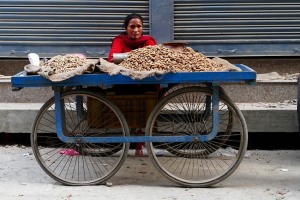 Donna appartenente all'etnia Gurung vende sul suo carrettino le arachidi tostate all'interno di un vaso di terracotta inserito in un barattolo di metallo con carbone, peroferia di Kathmandu, Nepal 2018.