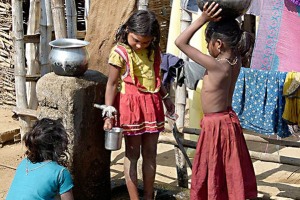 Queste tre bambine Kodavas chiaccherano amabilmente presso ll'unica fontana del villaggio: ognuna di loro svolge un compito ben preciso, una ha lavato e steso il bucato, un'altra ha riempito un contenitore di alluminio con l'acqua da portare a casa e l'ultima sta riempiendo un altro catino sempre di acqua. I loro nomi, da sinistra a destra, sono rispettivamente: Indira (uno dei nomi che identificano la Dea Lakshmi, nella mitologia hindu moglie di Narayan), Inay (simile a Dio), Denali (in lingua hindu significa "la donna che è grande"). Villaggio di Kakkabe, Distretto di Kodagu, Regione del Karnataka, India 2015.