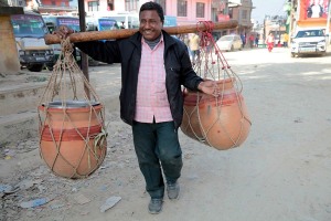 Un uomo Newari trasporta tre otri pieni d'acqua con l'ausilio di un lungo bastone posto sulle spalle sfruttando il baricentro del suo corpo: è la prima volta che incontro un uomo nepalese che svolge un'attività prevalentemente femminile, villaggio di Kirtipur, Nepal 2018.