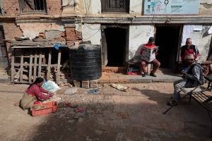 Mentre gli uomini Newari oziano seduti su sedie o panchine, una donna seduta a terra separa a mano la crusca dal grano, Villaggio di Kirtipur, Nepal 2018.