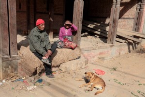 Due anziani coniugi Newari sono seduti sul portico della loro casa in fase di ricostruzione con accanto il loro fedele cane, villaggio di Kirtipur, Nepal 2018.