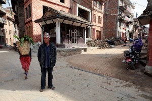 Una donna rientra dalla campagna con la grande cesta sulla schiena ("Doko") piena di ortaggi, mentre un uomo Newari mi scruta interrogativo, villaggio di Kirtipur, Nepal 2018.