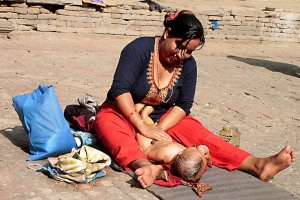 A lato della maestosa Durbar Square, nella città vecchia di Kathmandu, una mamma massaggia amorevolmente tutto il corpicino del suo neonato con olio profumato nel cortile interno della sua abitazione, dintorni di Makhan Tole (in nepali "strada di burro"), Nepal 2018