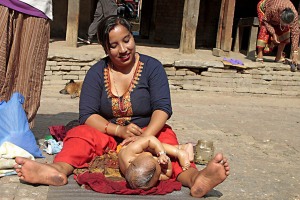 In un cortile interno a lato della maestosa Durbar Square, nella città vecchia di Kathmandu, una mamma massaggia amorevolmente tutto il corpicino della sua neonata con olio profumato, dintorni di Makhan Tole (in nepali "strada di burro"), Nepal 2018